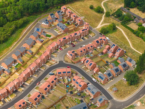 Aerial view of a modern residential new build suburb featuring rows of red brick houses with solar panels, paved streets, and gardens in Burton upon Trent, England, United Kingdom.