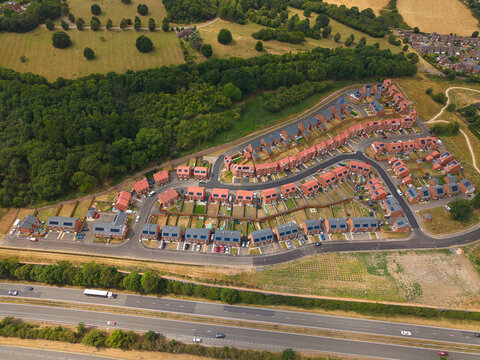 Aerial view of a modern residential new build suburb with rows of red brick houses, private gardens, and winding roads near a highway in Burton upon Trent, England, United Kingdom.