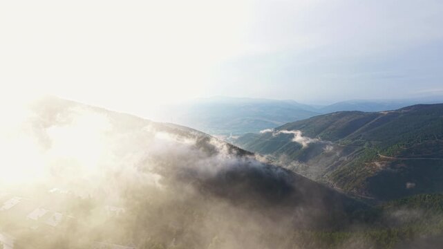 Low cloud inversion layer drifts over a forested mountain valley near La Molina, Catalan Pyrenees, Spain, with village rooftops visible below and layered ridges fading into misty distance