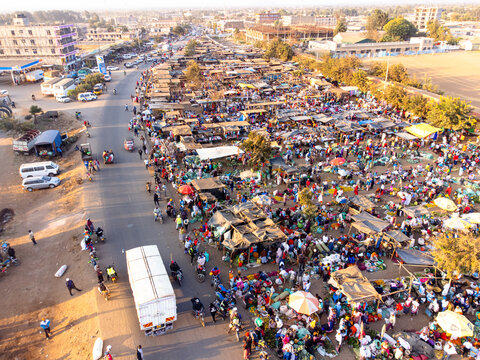 Aerial view of a bustling outdoor market in Kimana with numerous stalls, vendors, and shoppers, set against a backdrop of dusty roads and buildings in Kimana, Kajiado County, Kenya.