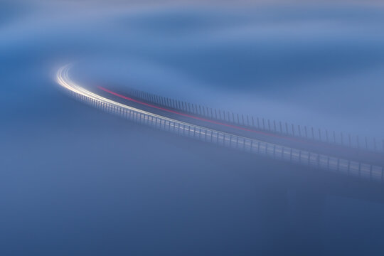 Aerial view of the Crni Kal Viaduct with long exposure light trails from vehicles moving through thick fog in Crni Kal, Koper, Slovenia.