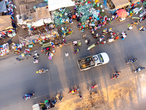 Aerial view of a bustling outdoor market with vendors, shoppers, motorcycles, and a pickup truck on a dusty road in Kimana, Kajiado County, Kenya.
