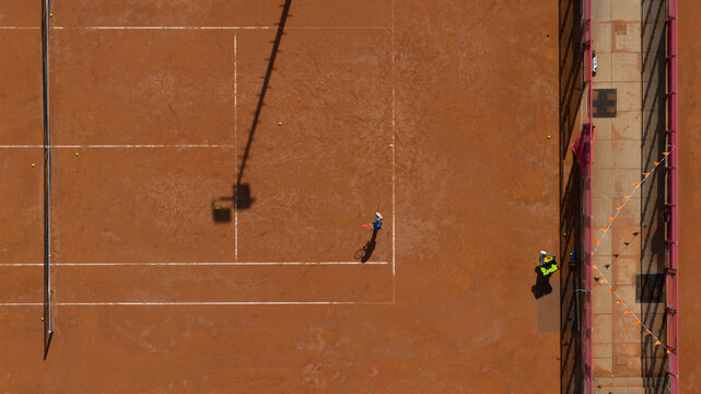 Aerial view of Tennisclub IJburg with a player on the clay court, white lines, and surrounding fencing in Amsterdam, Noord-Holland, Netherlands.