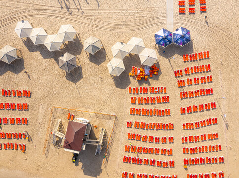 Aerial view of Tel Aviv Beach with rows of orange sun loungers, umbrellas, and a lifeguard tower on the sandy shore in Tel Aviv-Yafo, Tel Aviv District, Israel.