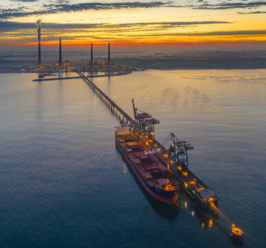 Aerial view of Orot Rabin Power Plant with a large cargo ship docked at the pier during a vibrant sunset in Hadera, Haifa District, Israel.