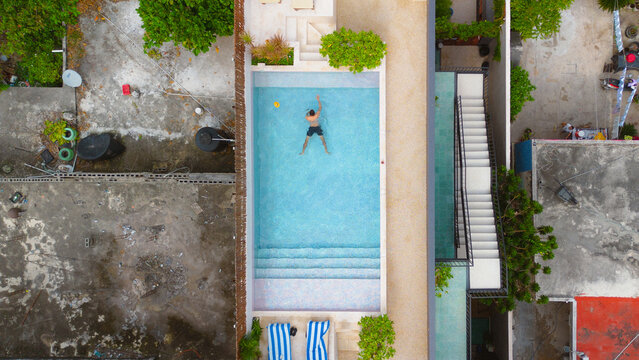 Aerial view of a man swimming in a turquoise pool at Poolside Tulum with modern architecture, stairs, and sun loungers in Tulum, Quintana Roo, Mexico.