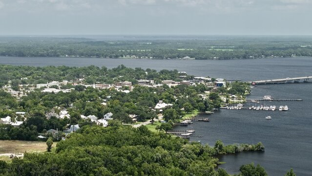 Aerial view of the city of Palatka along the St. Johns River featuring a bridge, marina with docked boats, and surrounding lush green trees in Palatka, Florida, United States.