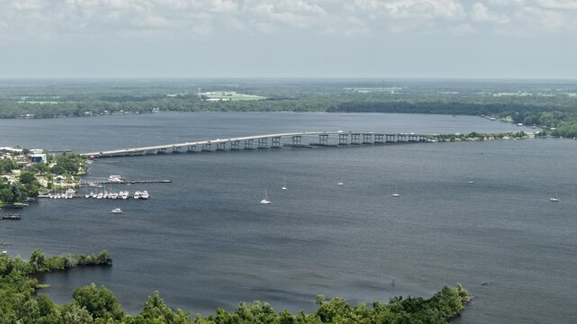 Aerial view of the Memorial Bridge spanning the St. Johns River with boats docked at the marina and lush green trees along the shoreline in Palatka, Florida, United States.