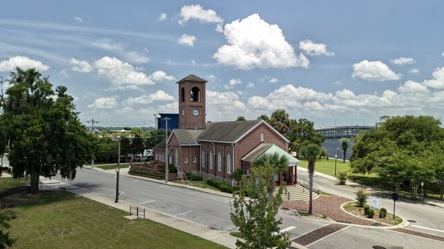 Aerial view of St. Mark's Episcopal Church with its distinctive clock tower and red brick architecture, surrounded by lush trees and nearby river in Palatka, Florida, United States.