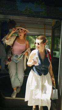 Happy tourists alight from a public bus, ready to explore their summer travel destination with a map. A young woman and man smile, enjoying their vacation adventure after disembarking from transport.
