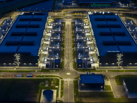 Aerial view of a large illuminated data center complex at night featuring symmetrical buildings, cooling infrastructure, and a central roundabout in Middenmeer, North Holland, Netherlands.