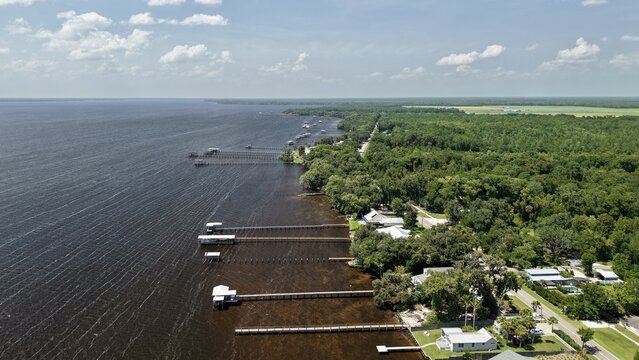 Aerial view of Riverdale Park and boat ramp with wooden piers extending into the dark water, surrounded by lush green trees and coastal vegetation in St. Augustine, Florida, United States.