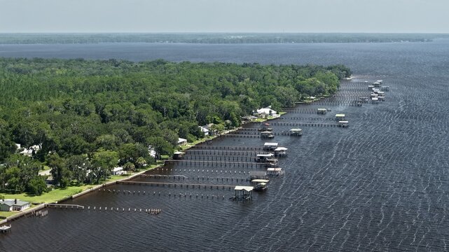 Aerial view of Riverdale Park and boat ramp with wooden docks extending into the St. Johns River, surrounded by lush trees and residential houses in St. Augustine, Florida, United States.