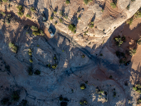 Aerial view of off-road vehicles navigating rocky desert terrain with sparse vegetation and rugged sandstone formations in Moab, Utah, United States.