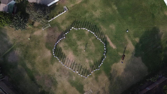 Aerial view of a group of people standing in a large circle on a grassy field, casting long shadows during a company integration event in Lima, Callao Region, Peru.