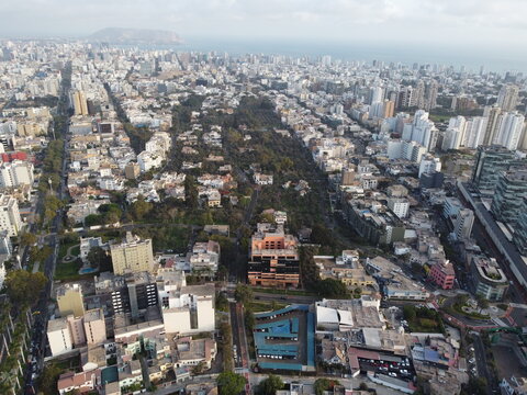 Aerial view of Bosque El Olivar surrounded by dense urban buildings and high-rise architecture in San Isidro, Provincia de Lima, Peru.