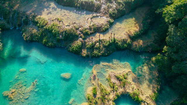 Aerial view of Semuc Champey featuring turquoise limestone pools surrounded by lush jungle with people swimming in the clear water, San Agustin Lanquin, Alta Verapaz Department, Guatemala.