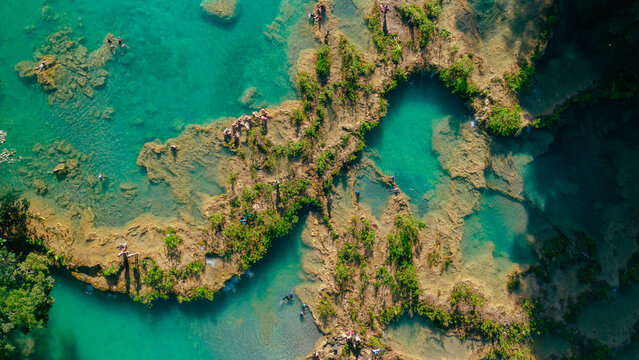 Aerial view of Semuc Champey featuring turquoise limestone pools surrounded by lush tropical vegetation with people swimming in the clear water in San Agustin Lanquin, Alta Verapaz, Guatemala.