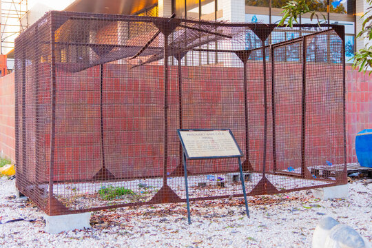 Lusaka, Zambia - 01 July 2026: View of a historical prisoner wire cage exhibit made of rusted metal mesh, standing on a gravel ground against a red brick wall.