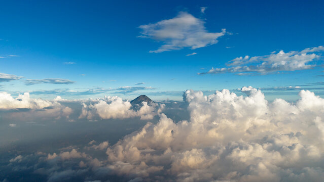 Aerial view of the peak of Acatenango volcano rising above a sea of thick white clouds under a clear blue sky in Alotenango, Sacatepequez Department, Guatemala.