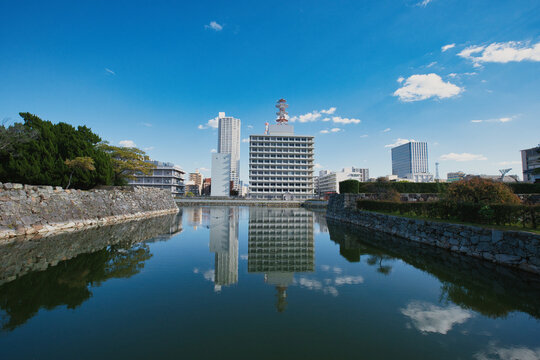 Hiroshima, Hiroshima, Japan - 15 November 2025: View of the historic stone walls and moat surrounding the Hiroshima Castle grounds, reflecting the modern city skyline under a clear blue sky.