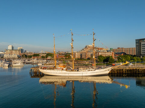 Aerial view of the tall ship BAE Guayas docked in the harbor with city buildings in the background under a clear blue sky in Boston, Massachusetts, United States.