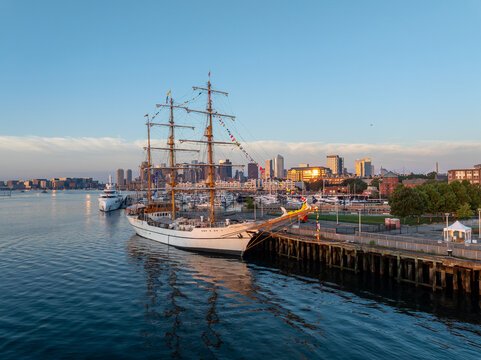 Aerial view of the tall ship BAE Guayas docked in the harbor with the city skyline in the background during golden hour in Boston, Massachusetts, United States.