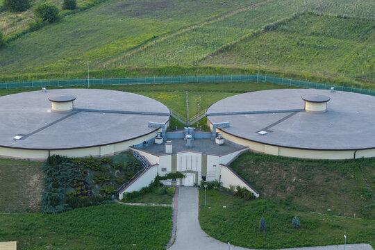 Aerial view of a water treatment plant featuring two large circular tanks and a central facility surrounded by green grassy hills in Dobczyce, Lesser Poland Voivode, Poland.