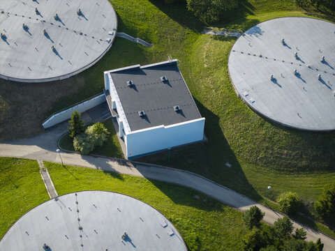 Aerial view of a water treatment facility featuring large circular storage tanks, a central building, and surrounding green grassy slopes in Dobczyce, Lesser Poland Voivode, Poland.