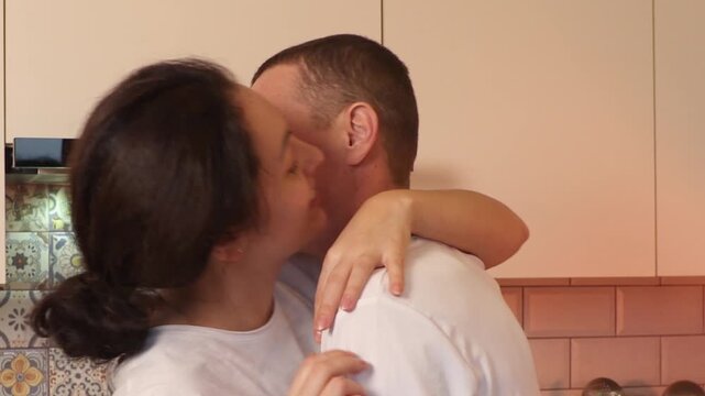 Attractive young man and woman dancing together in a cozy kitchen filled with warmth. They smile, flirt, and celebrate simple everyday moments that strengthen their emotional bond. Mid shot