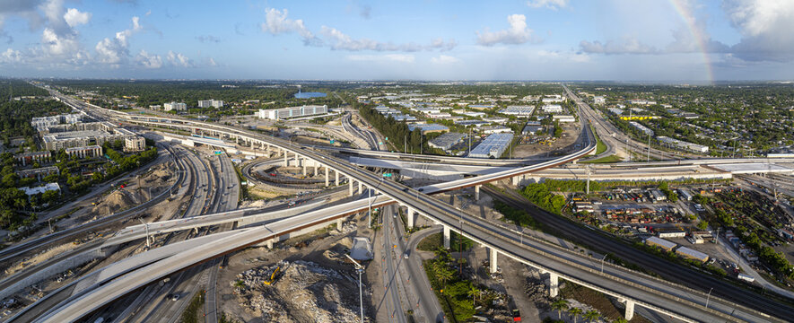 Aerial view of the Golden Glades Interchange featuring complex highway overpasses, surrounding urban infrastructure, and a faint rainbow in the sky in Miami, Florida, United States.