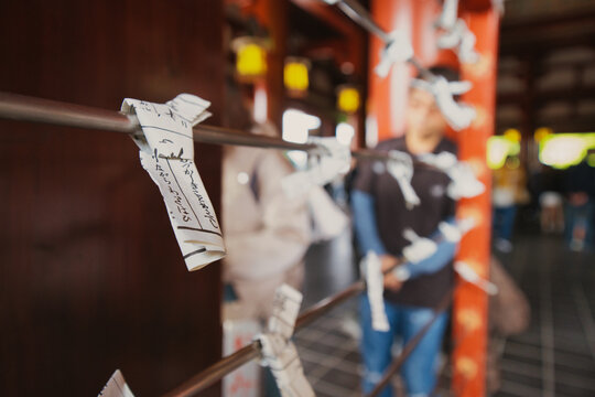 Tokyo, Japan - 01 November 2025: View of paper fortunes known as omikuji tied to a metal rack at a traditional shrine in Tokyo, Japan, with a blurred visitor in the background.