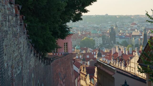 Historic brick wall stands above red tile roofs in Prague. Scenic urban panorama shows classic Old Town architecture in warm sunlight. Ideal scene for European travel and tourism content.