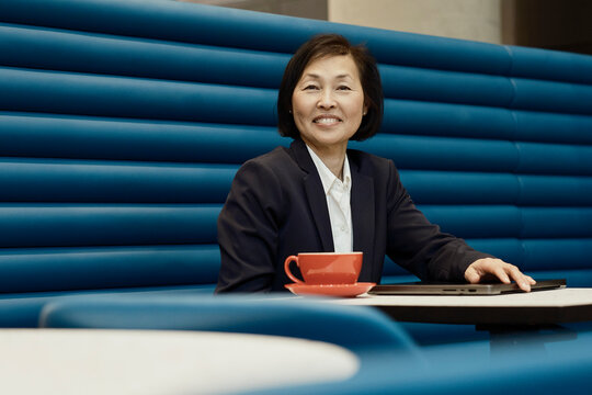 Smiling businesswoman sits with coffee and laptop at the office