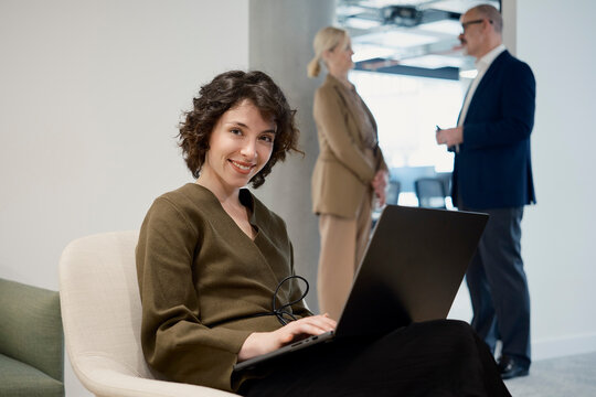 Smiling businesswoman uses laptop while colleagues chat in office