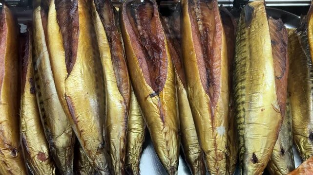 Cold smoked salmon balyk on counter, close-up of hanging golden fillets with visible salt crystals on metal rack inside fish shop