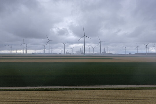 Aerial view of a wind farm with numerous turbines set against agricultural fields under a cloudy sky in the Netherlands.