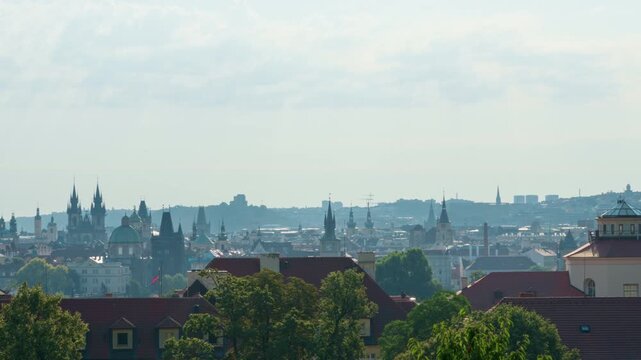 Panoramic Prague cityscape reveals historic church spires and roofs in soft morning haze. Zizkov television tower rises on the horizon. Scenic landscape showcases Czech travel and urban heritage.