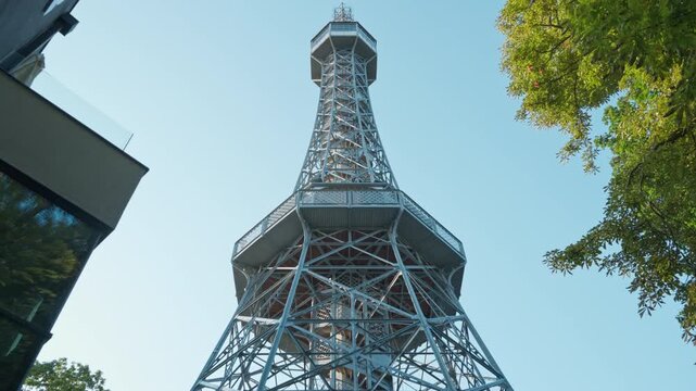 Steel Petrin lookout tower stands among green trees in Prague. Historic metal lattice structure symbolizes Czech engineering, urban architecture, European tourism, and summer holiday travel.