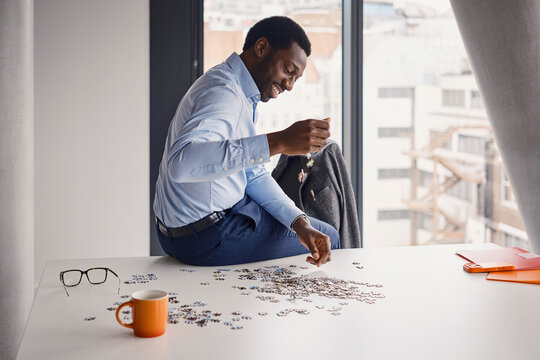 Smiling businessman drops jigsaw puzzle pieces on an office desk