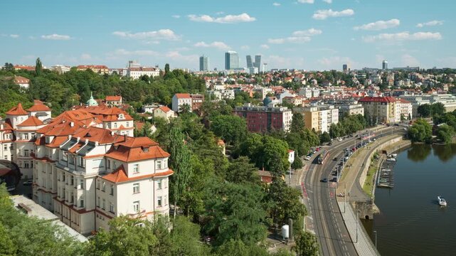 Prague city panorama overlooks the Vltava river with red roof houses and boat marina. Modern skyline rises on horizon in sunny daylight. Great scene for European travel and urban tourism.