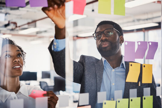 A man and woman brainstorm business ideas on an office glass wall