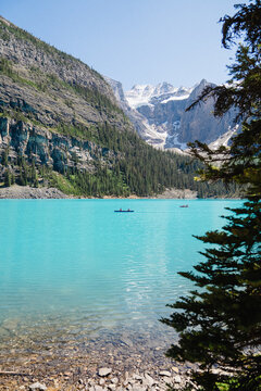 View of Moraine Lake with its iconic turquoise water, surrounded by towering rocky mountains, pine forests, and a canoe with people paddling in Improvement District No. 9, Alberta, Canada.