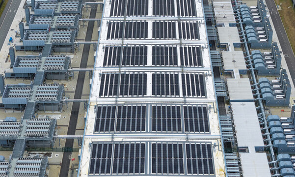 Aerial view of a large data center facility featuring extensive solar panel arrays on the roof and complex industrial cooling infrastructure in Winschoten, Netherlands.