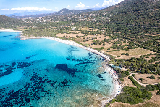 Aerial view of Plage de Ghjunchitu with turquoise waters, sandy beach, and Mediterranean vegetation along the rocky coastline in Corbara, Corse, France.