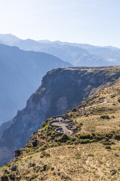 View of the winding stone viewing platform at Colca Canyon with people standing on the edge of the deep gorge surrounded by arid mountainous terrain in Arequipa, Arequipa, Peru.