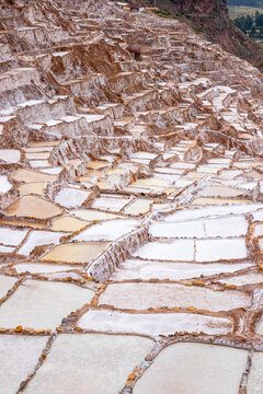 View of the historic Maras Salt Mines featuring numerous terraced salt evaporation ponds carved into the mountainside in Maras, Cusco, Peru.