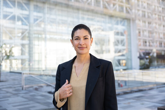Confident businesswoman stands outdoors near a modern office building