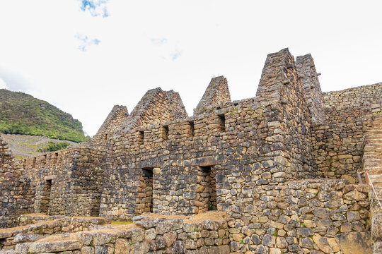 View of the ancient stone ruins of Machu Picchu with gabled walls and intricate masonry under a bright sky in Machu Picchu, Cusco, Peru.