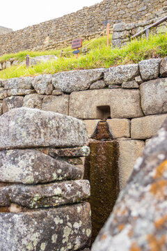 View of the ancient Inca stone water channel at Machu Picchu with mossy masonry and flowing water in the historic site of Machu Picchu, Cusco, Peru.
